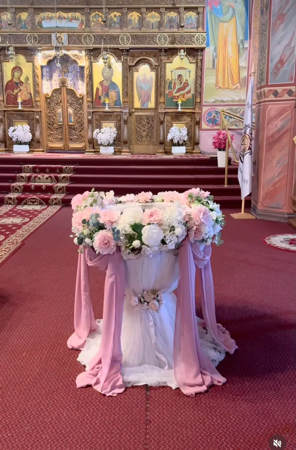 Fotografie a cristelniței decorate cu flori roz și albe și voaluri roz, în biserică.