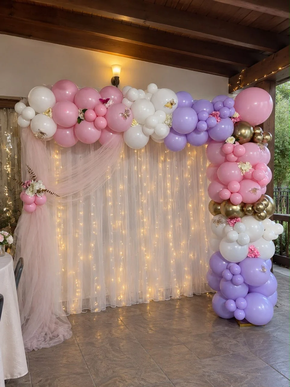 Decor real cu fundal din voal, luminițe și baloane roz, albe, lila și aurii.